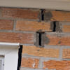A brick wall displaying stair-step cracks and messy tuckpointing on a Ithaca home
