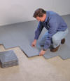 Contractors installing basement subfloor tiles and matting on a concrete basement floor in Clay, New York
